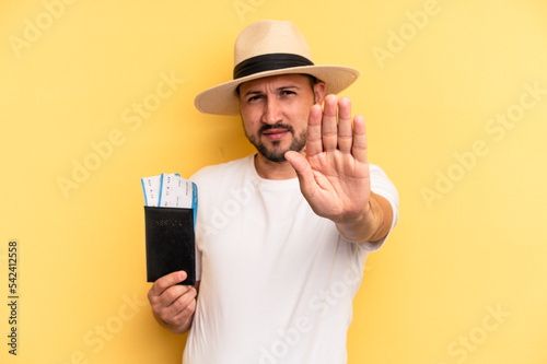Young latin man holding a flight tickets for vacations standing with outstretched hand showing stop sign, preventing you.