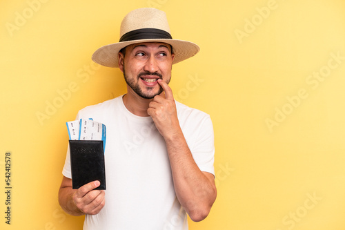 Young latin man holding a flight tickets for vacations relaxed thinking about something looking at a copy space. © Asier