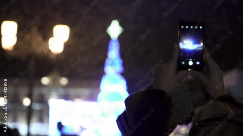 Slow motion handheld shot of a person using their smartphone to film a glowing christmas tree with a star on top in medina sidonia in spain during beautiful snowfall Slow motion handheld shot of a person using their smartphone to film a glowing christmas tree with a star on top in medina sidonia in spain during beautiful snowfall