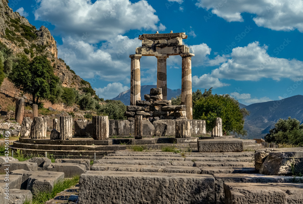 Enduring ruins of a Greek temple with the dome of Delphi, dating from the 4th century BCE in Greece with Doric columns cloudy blue sky