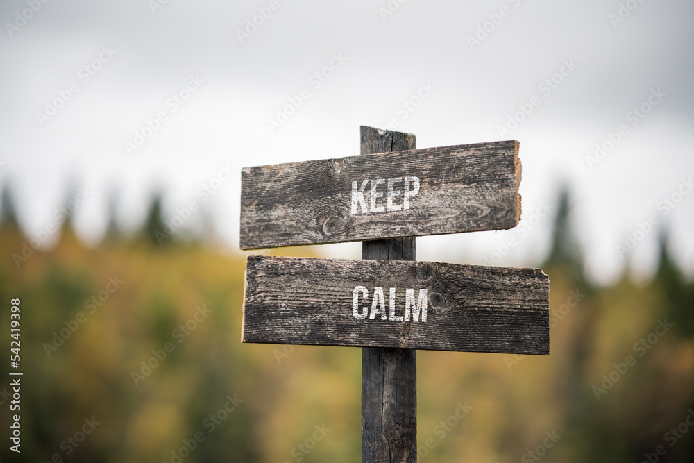 vintage and rustic wooden signpost with the weathered text quote keep calm, outdoors in nature. blurred out forest fall colors in the background.