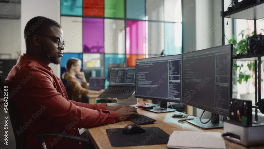 African American Man Writing Code on Desktop Computer With Multiple Monitors Set Up and a Laptop in Creative Office. Professional Data Scientist Using Software to Analyze Information From Internet. African American Man Writing Code on Desktop Computer With Multiple Monitors Set Up and a Laptop in Creative Office. Professional Data Scientist Using Software to Analyze Information From Internet.
