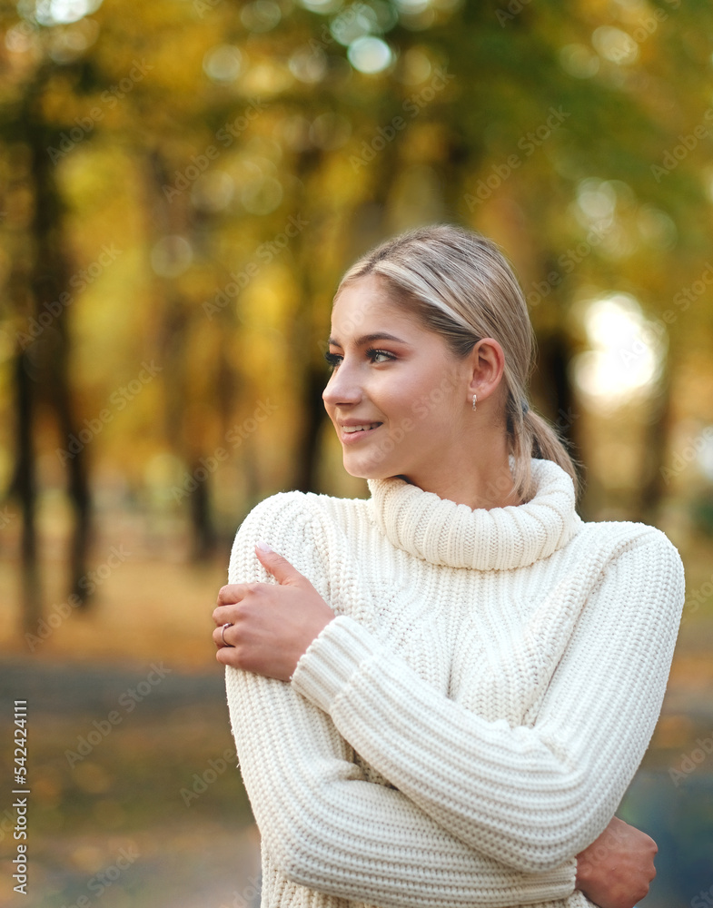 Young beautiful blonde woman in a white sweater walks in the autumn park.