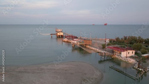 Slow-motion aerial view of fishing huts on shores of estuary at sunset,italian fishing machine, called 