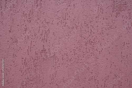 Closeup of plastered exterior wall painted in mauve purple color. Indented texture background.