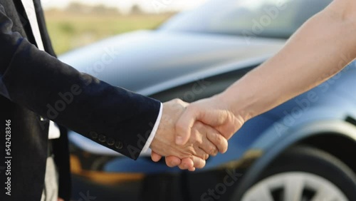 Man giving keys of car to buyer. Men shaking hands in electric car dealership on background of bought cars. Businessman giving car key to a caucasian man in automotive dealership showroom.