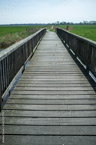 Pedestrian bridge passes over a moat filled with water, against the backdrop of fields.