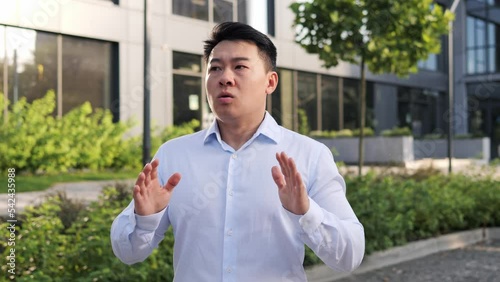 Asian businessman in blue shirt trying to calm down, breathing problems, chest pain outdoor. The man takes a deep breath and waves his hands to regulate his breathing. Finance problems at work. photo