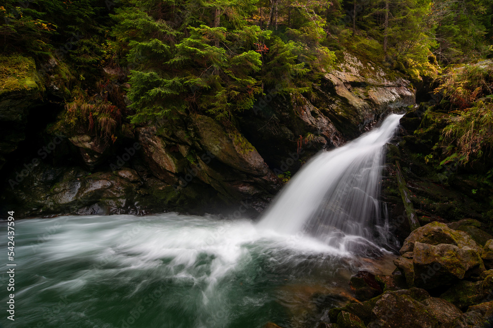 Naklejka premium Waterfall flowing through rocks in a deep forest, autumn landscape
