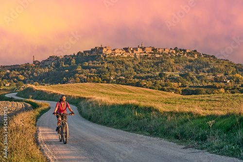 nice senior woman riding her electric mountain bike between olive trees in the Ghianti area with medieval city of Montepulciano in background, Tuscany , Italy photo