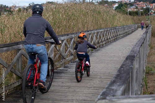 A father and his young son ride a bicycle along the wooden promenade of Panxon beach in Pontevedra photo