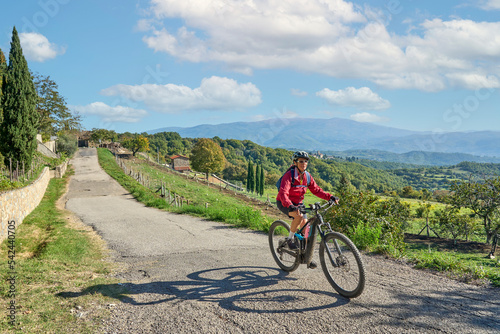 nice senior woman riding her electric mountain bike between olive trees in the Casentno hills near Arezzo,Tuscany , Italy