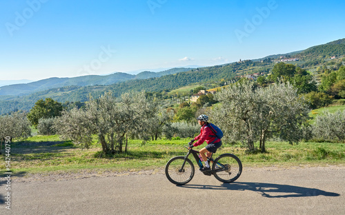 nice senior woman riding her electric mountain bike between olive trees in the Casentno hills near Arezzo,Tuscany , Italy