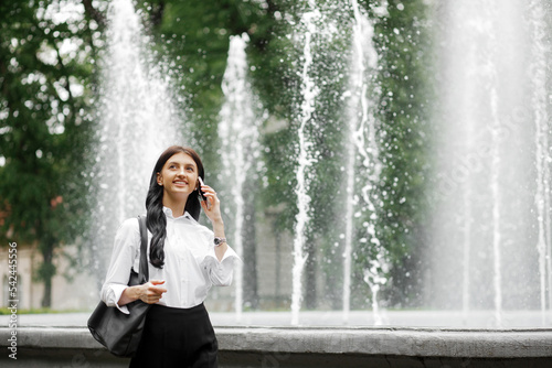 Busy caucasian girl talking on the phone on the background of a fountain in the park. Freelance concept.
