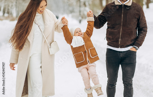 Happy family, young parents lift their daughter holding her hands on both sides. Walking in the winter park..Happy childhood.