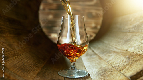 Pouring rum into glass inside old wooden barrel.