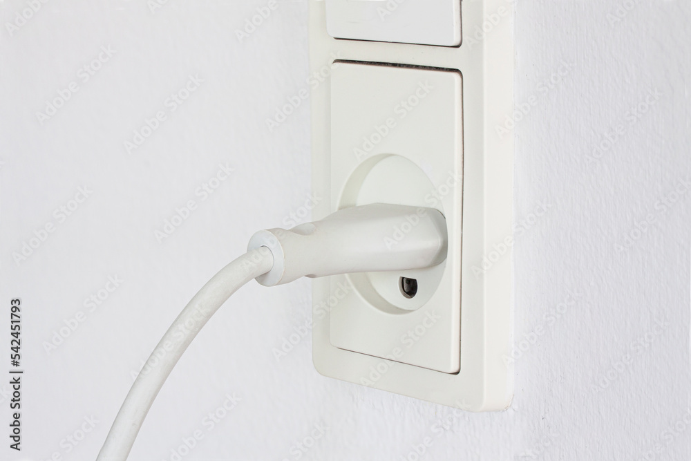 Close up of plug from an electrical appliance plugged into an electrical outlet on a white wall background. Power outlet white with cord. Electricity and power concept. Close up of plug from an electrical appliance plugged into an electrical outlet on a white wall background. Power outlet white with cord. Electricity and power concept.