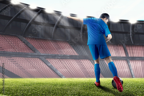 Rear view of a football player man in a blue jersey kicking the ball © Leo Lintang