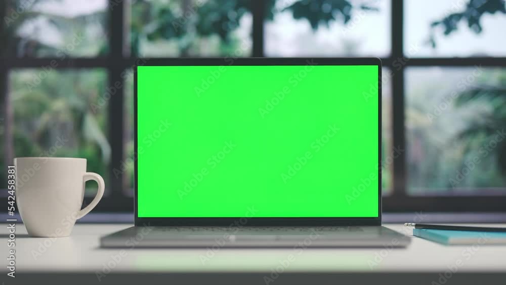 Home workplace with laptop and cup of coffee, desktop computer before window and trees view with chroma green screen of copy space