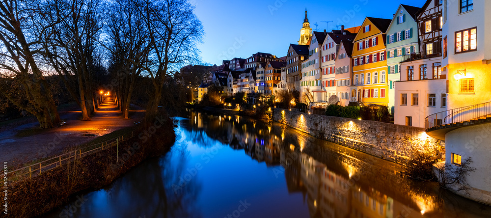 Panoramic view of old town houses in Tübingen Germany. Colorful facades mirroring in Neckar river on a winters day at blue hour evening twilight. Picturesque tourist attraction called “Neckarfront“.