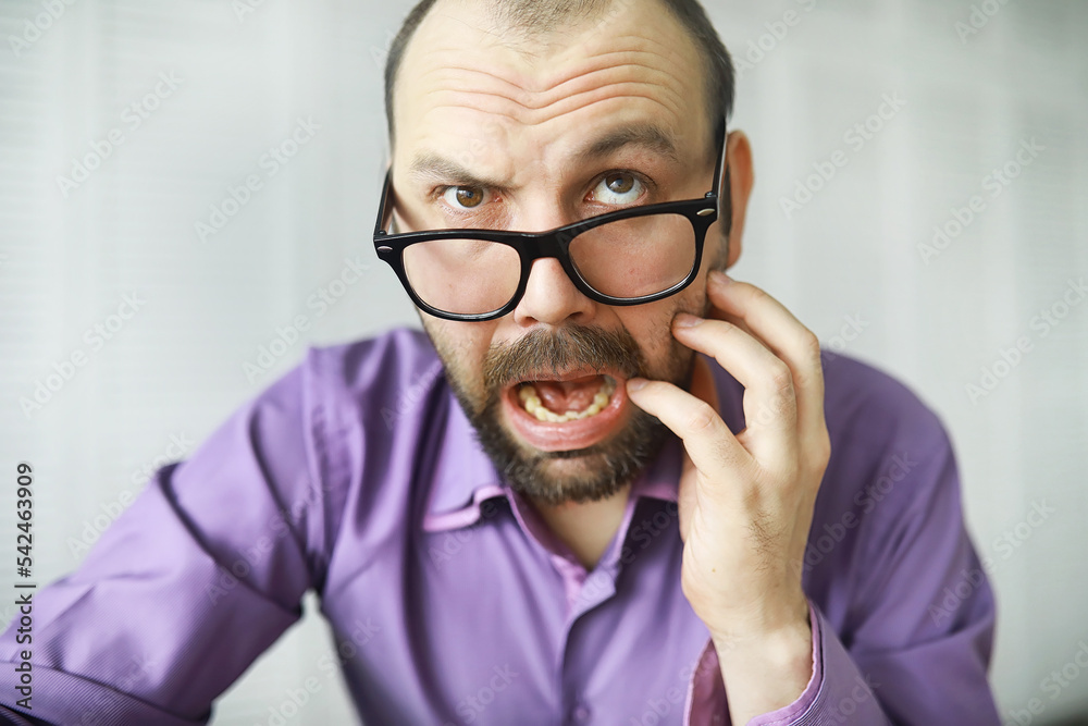 A cross-eyed bearded man is looking into the frame. Eye disease. The concept of an inexperienced specialist. Spy neighbor. A cross-eyed bearded man is looking into the frame. Eye disease. The concept of an inexperienced specialist. Spy neighbor.