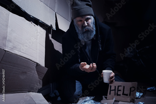A homeless bearded man sits on boxes on the street and asks for help. Need a homeless person asks for money for food and overnight. photo