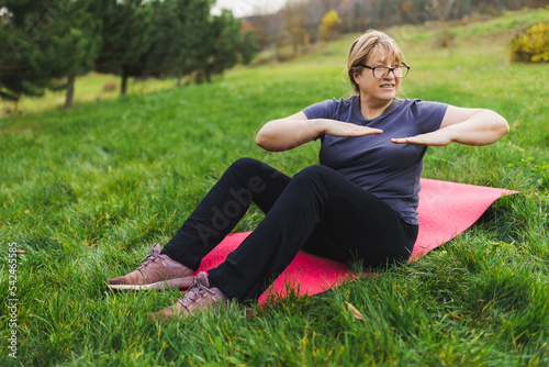 Mature caucasian retired woman in the park meditates and performs breathing exercises, summer day