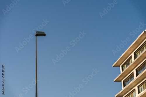 Low-angle view of a lamp column by a residential building under the blue sky