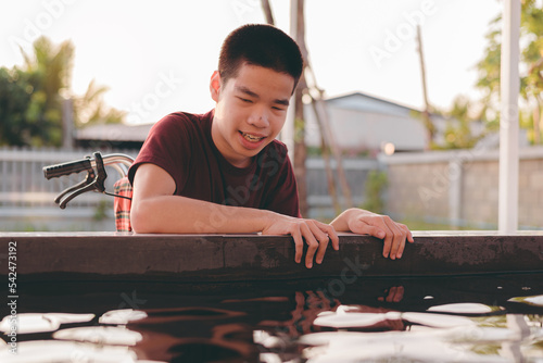 Teenager boy with a disability looking and feeding fish in pond with smile and happy face, Training of muscles through picking,Animals therapy,Outdoor ativity,Rehabilitation and Mental Health concept. photo