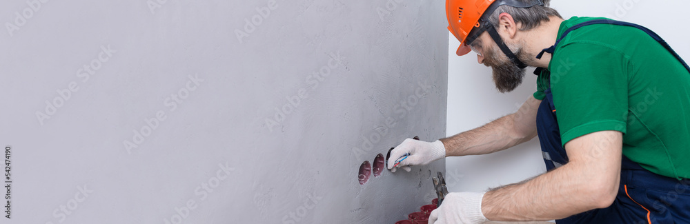 An electrician installs sockets in the apartment. A guy in an orange helmet and overalls makes electrics in the house. An electrician installs sockets in the apartment. A guy in an orange helmet and overalls makes electrics in the house.