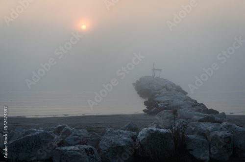 Un frangiflutti della spiaggia del Lido di Venezia con il sole che sorge in una nebbiosa giornata autunnale