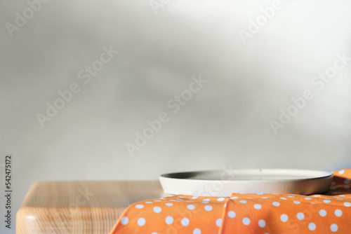 Empty concrete plate on orange tablecloth on wooden table over grunge grey background. side view. copy space for food placement
