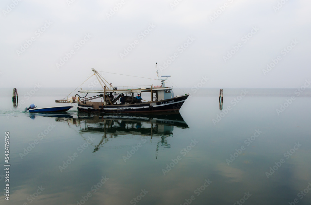 Un peschereccio naviga nelle acque tranquille della laguna di Venezia davanti all'isola di Pellestrina in una nuvolosa giornata invernale 