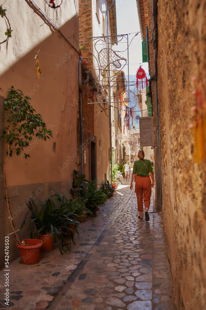 Mujer de espaldas camina en una calle de colores cálidos de un pueblo pintoresco en el Mediterráneo