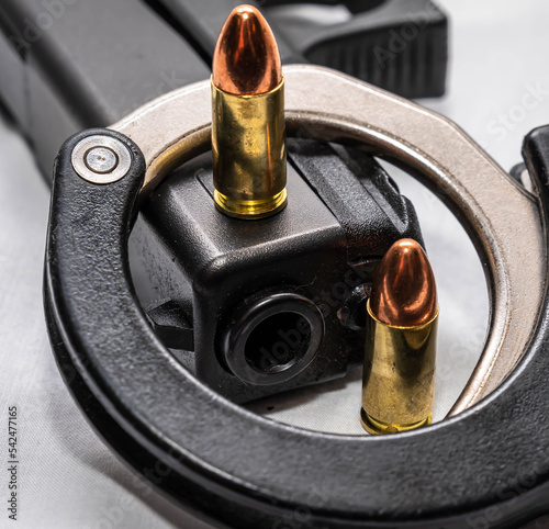 Two 9mm full metal jacket bullets with a black 9mm pistol and a half of a set of handcuffs on a white background