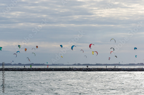 Le vele di numerosi kitesurfers si muovono nel cielo sopra la spiaggia di Chioggia in una ventosa giornata autunnale photo