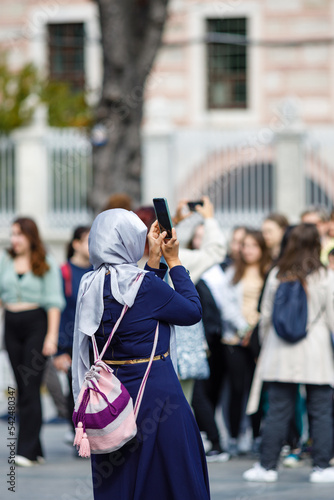Islamic woman taking photos on phone, back view. Shooting video with cell phone camera, using smartphone to take pictures outdoor. Tourist photographing landscape. Sightseeing concept