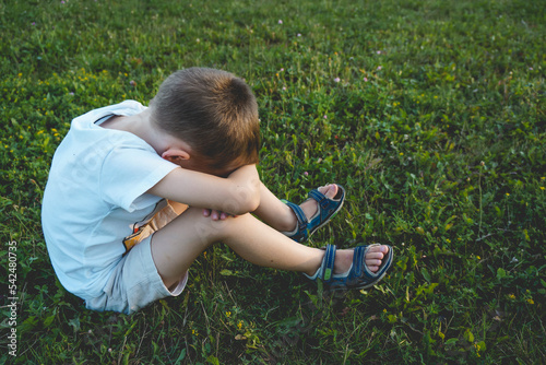 Boy is sitting on the grass and covering face with his hands photo