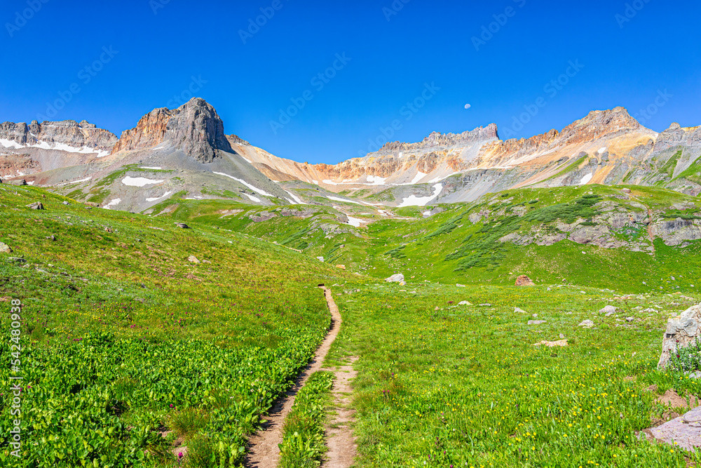 Open landscape wallpaper view of green grass meadow field and trail footpath road to Ice lake near Silverton, Colorado in August summer with clear blue sky