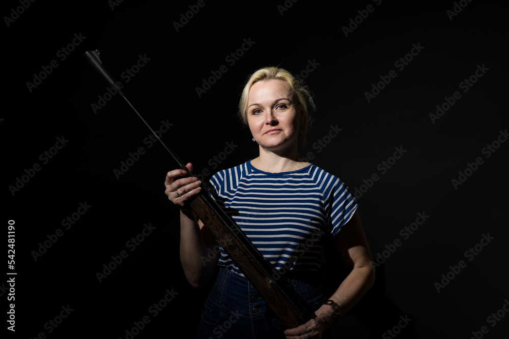 an adult woman in a vest with a rifle in her hands stands in the dark an adult woman in a vest with a rifle in her hands stands in the dark
