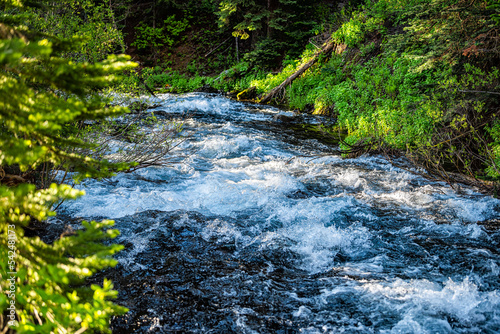 West Maroon creek river blue color water near Maroon bells lake in Aspen, Colorado with closeup of white water flowing in summer by forest of lush green foliage photo