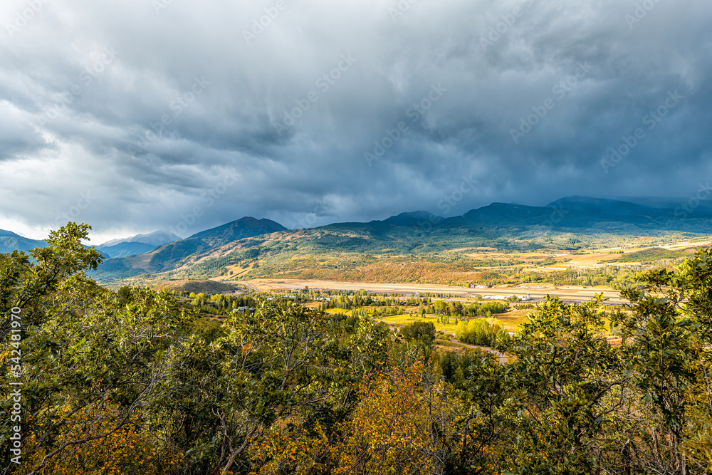 Wide angle view of Aspen, Colorado Rocky mountains at storm stormy sunset with cloudy clouds sky of blue skyscape by oak trees in foreground
