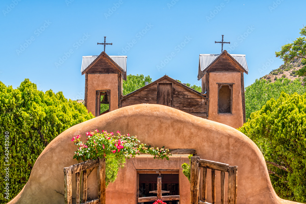 Obraz premium Famous historic adobe El Santuario de Chimayo sanctuary church in the United States with entrance gate closeup of flowers in summer