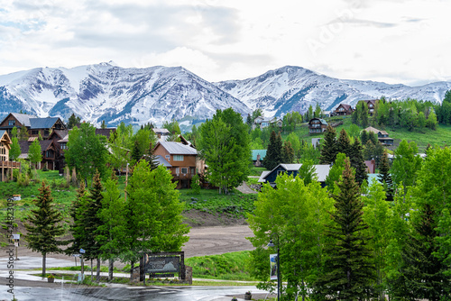 Mount Crested Butte, Colorado small village ski resort town in summer with cloudy sunrise morning and houses on hills with green trees and main street sign