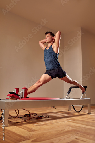 Side view of barefoot male athlete lying on pilates reformer and performing abs exercise during fitness workout. Pilates man concept.