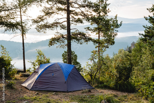 A gray tent stands in the forest against the background of a mountain, a morning dawn in a campsite, camping equipment, a place to sleep in nature, rest in the forest.