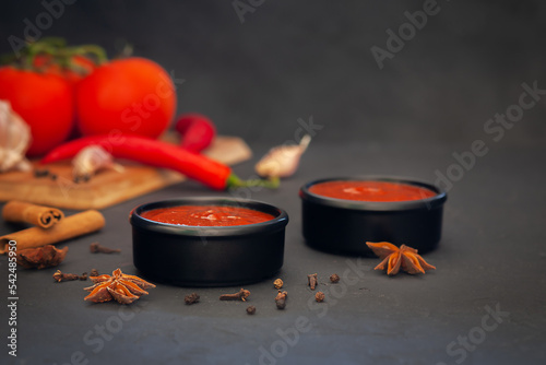 Delicious ketchup in a bowl with ingredients on the background