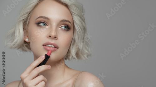 Close-up portrait of a beautiful girl using pink lipstick. Gray background.