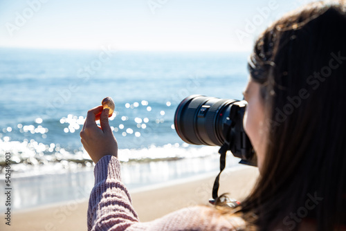 Beautiful woman taking a picture of a sea shell holding it with her hand