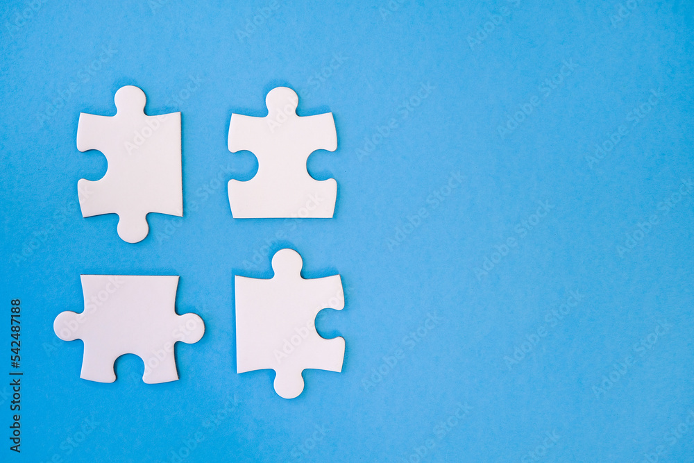 Obraz premium Four whiie jigsaw puzzle pieces on blue background ready to be fitted togther with negative space for copy.
